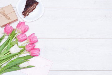 Bouquet of pink tulips, chocolate cake. pressent box on white wooden background. Copy space, close up. Mother's, women's day concept. Flat lay.