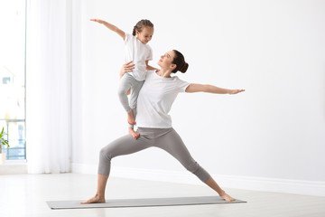 Young mother with little daughter practicing yoga at home