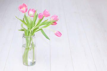 Pink tulips bouquet in glass vase on white wooden background. Copy space. Spring background, holiday, birthday concept.