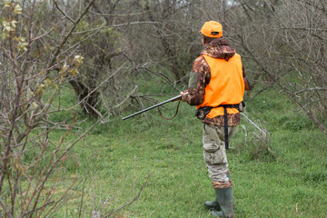 A man with a gun in his hands and an orange vest on a pheasant hunt in a wooded area in cloudy...