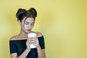 Young pretty woman with take away coffee cup. Young girl at yellow background, copy space...