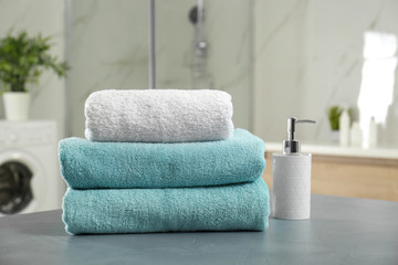 Fototapeta na wymiar Stack of clean towels and soap dispenser on grey stone table in bathroom