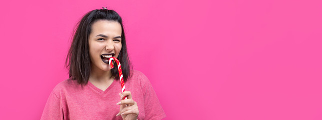 Portrait of lovely sweet beautiful cheerful woman with straight brown hair trying to bite red candy cane christmas.