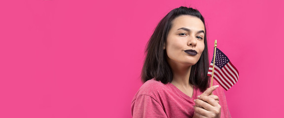 Happy young woman holding American flag against a studio pink background