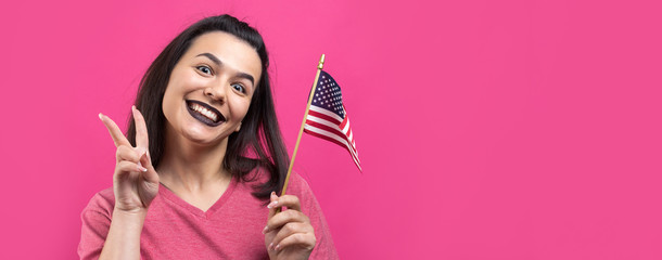 Happy young woman holding American flag against a studio pink background