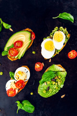 Sweet potato toasts with avocado, boiled eggs, tomatoes and sesame seeds on dark background. Healthy meal concept. Clean eating, Pescetarian food, top view