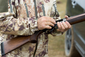 Charges a hunting smooth-bore rifle, hunting a pheasant with dogs. A hunter in camouflage is standing with a weapon.