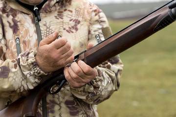 Charges a hunting smooth-bore rifle, hunting a pheasant with dogs. A hunter in camouflage is standing with a weapon.