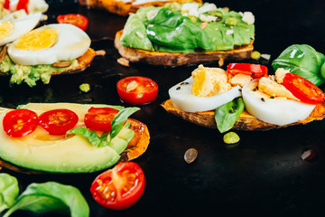 Sweet potato toasts with avocado, boiled eggs, tomatoes and sesame seeds on dark background. Healthy meal concept. Clean eating, Pescetarian food, top view