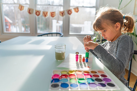 Young girl painting colorful wooden doll models of her family