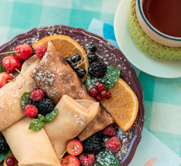 Fresh pancakes with berries. Pancakes with berries of forest fruits on brown plate. Blueberries, raspberries, cherries, currants, orange and mint leaf on pancakes are decorated. Top view food photo