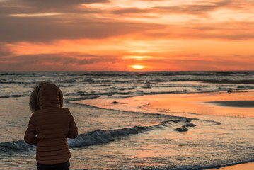 Unrecognizable girl from behind with a yellow jacket on a beach during sunrise