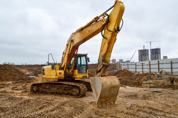 Big bright yellow powerful industrial heavy excavator tractor, bulldozer, specialized construction equipment for road repair during the construction of a new micro-district in a big city