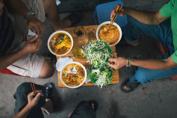 High angle close up of three men tucking into bowls of noodles for breakfast in a small alleyway.,Danang
