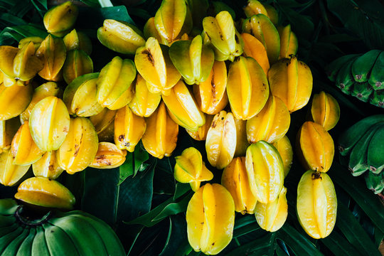 Close up of star fruits and green bananas for sale along the side of the road.