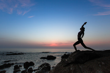 Silhouette of woman doing yoga exercises on ocean beach at evening.