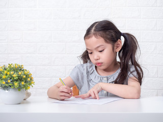 Asian little cute girl 6 years old seriously thinking about math homework over white brick wall...