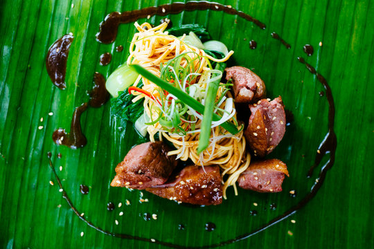 High angle view of seared duck breast and noodles served on a banana leaf.,Saigon