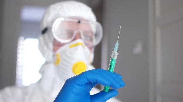 Close portrait of a man in a protective suit, in a mask and a respirator is preparing an injection for a patient with a coronavirus. Medical research, coronavirus vaccine