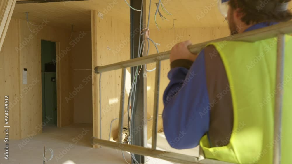 Wall mural SLOW MOTION, CLOSE UP: Builder leaves the construction site with his toolbox and ladder in hand. Worker coming to work carries his metal toolbox and ladder across the room of a prefabricated house.