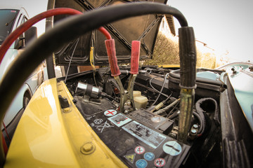 A pair of jumper or starter cables connected to a dead battery in a yellow vintage car. Concept of roadside assistance on old cars.