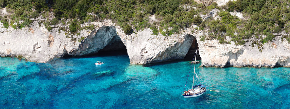 Aerial drone ultra wide photo of breathtaking turquoise exotic bay of blue lagoon in island of Paxos visited by sail boats, Ionian, Greece