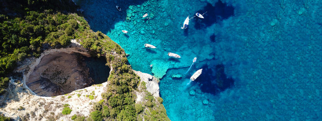 Aerial drone ultra wide photo of tropical white rocky bay of blue lagoon with turquoise clear waters, white volcanic caves and sail boats docked, island of Paxos, Ionian, Greece