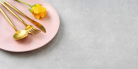 Top view of pink plate and gold cutlery on grey background