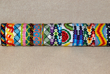 Colorful braided friendship bracelets handmade of thread on stand for sale isolated on beige background with copy space