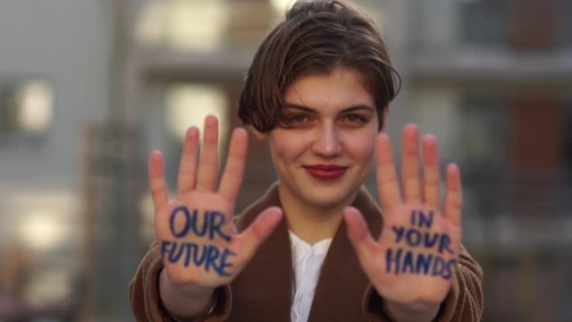 Climatic strike. A young girl with a short haircut with an inscription on her hand - our future is in your hands. Global climate change. Holds out his hands in front of her