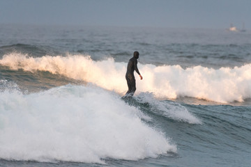 Unrecognizable surfer on the crest of the wave with his back to the camera