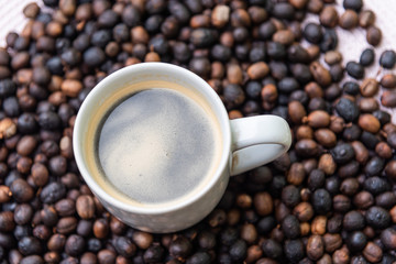 Cup of hot coffee in the middle of roasted coffee beans ready for grinding