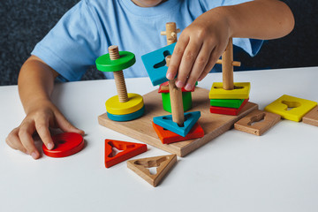 Child plays Montessori game. Kid collects wooden toy sorter. Multicolored geometric shapes, circle, square, triangle, rectangle.  Early childhood development