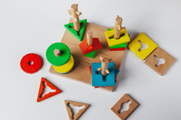Obraz premium Child plays Montessori toy. Multicolored logic sorter on white background. Baby Hands close-up. Wooden geometric shapes circle, square, triangle, rectangle. View from above
