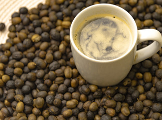 Cup of hot coffee in the middle of roasted coffee beans ready for grinding
