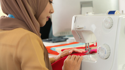 sewing machine in operation with hands of muslim dressmaker in hijab controlling at muslim dressmaker shop
