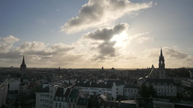 Cloudy sky over the city of Caen, Normandy, France. View on the roofs from the city's castle. Sun in front of the camera. Filmed in the winter just before the night.