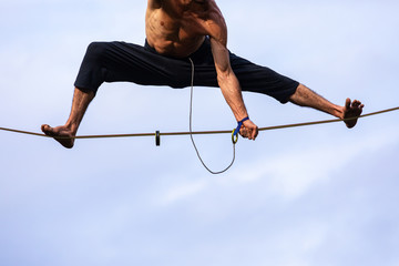 A low angle shot of a healthy caucasian man showing core strength and stability during a tightrope walk performance against a cloudy sky. Copy space below
