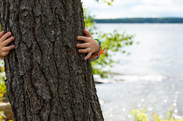 child hiding behind tree with camp bracelets on in front of lake