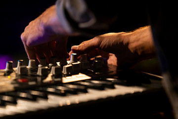 A close up selective focus shot on the hands of a man playing an electronic keyboard, turning dials...