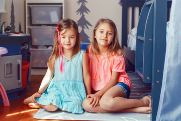 Two cute little Caucasian girls siblings sitting on floor at home room. Happy smiling friends relationship concept. Adorable children playing together. Authentic candid lifestyle domestic life moment.