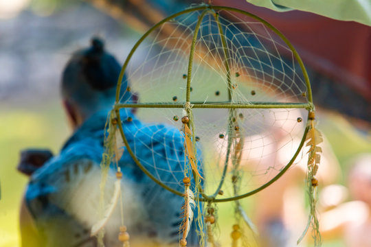 A soft selective focus shot of a sacred dreamcatcher hanging from tent during a festival celebrating culture and earth, with blurry man in background