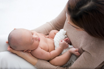 Beautiful mom supports and tenderly cuddles the newborn baby gently while the infant is sleeping on...