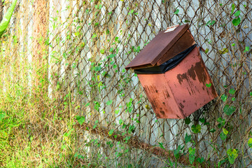 Red metal bin hang on a mesh fence in the garden.