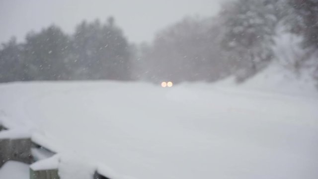 A defocused small SUV drives through hazardous snowy conditions in slow motion.