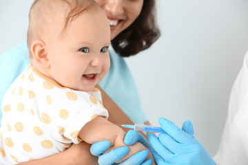 Pediatrician vaccinating little baby on light background