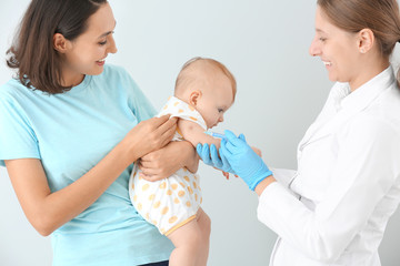 Pediatrician vaccinating little baby on light background