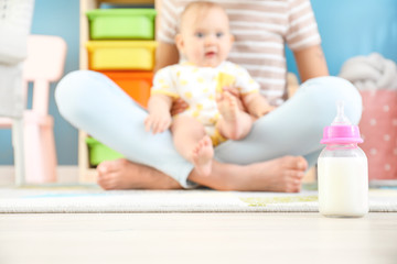 Mother with little baby and bottle of milk on floor
