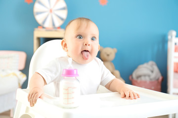 Baby with bottle of milk sitting in high-chair at home