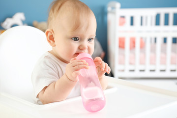 Baby with bottle of water sitting in high-chair at home